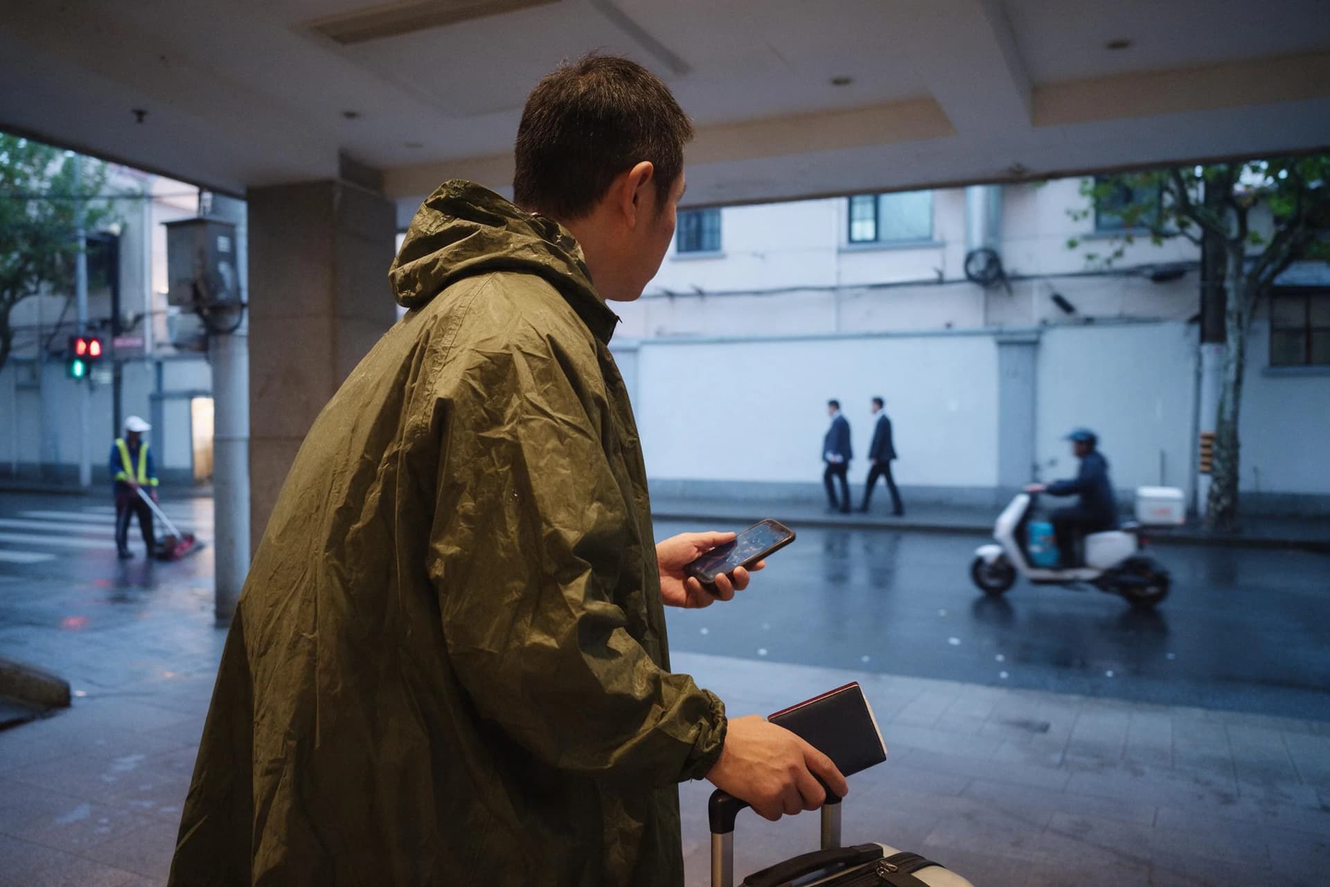 Solo business traveler with a passport wallet outside a Shanghai hotel on a rainy October morning