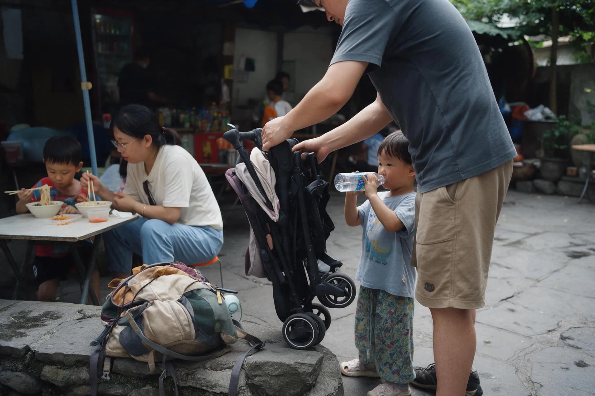 Family packing for China travel with a compact stroller, daypack and children at a courtyard snack shop