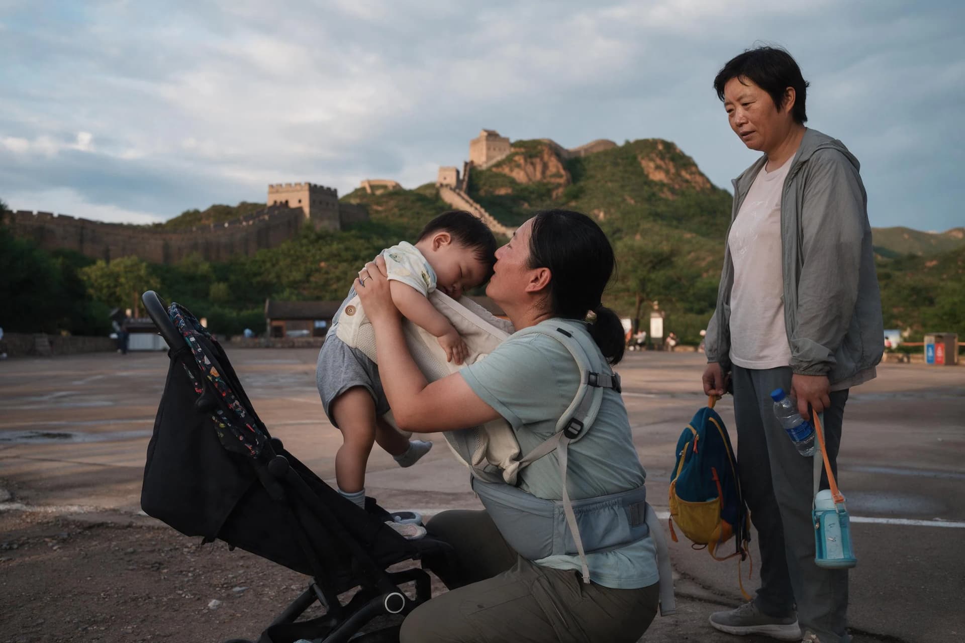 Parent lifting a toddler into a child carrier beside a stroller at the Great Wall at Jinshanling visitor area
