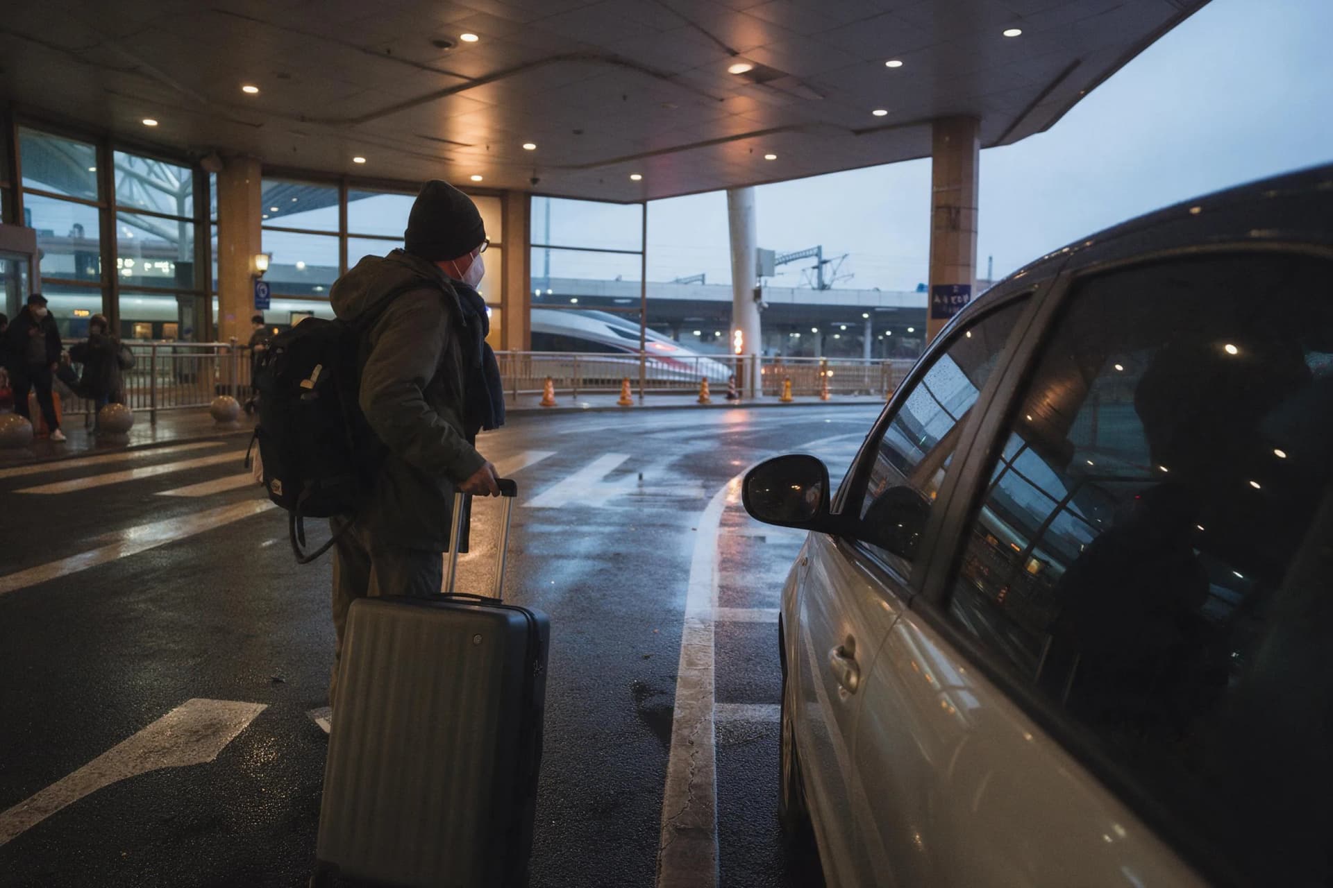 Private car waiting outside Beijing railway station beside a high-speed train at dawn
