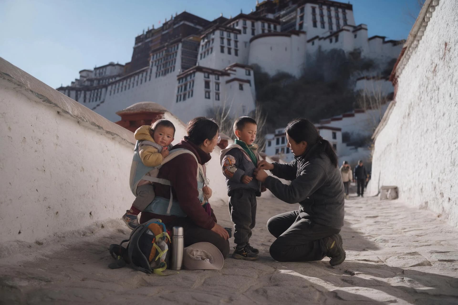 Family with a toddler in a carrier resting below the Potala Palace in Lhasa on a clear morning