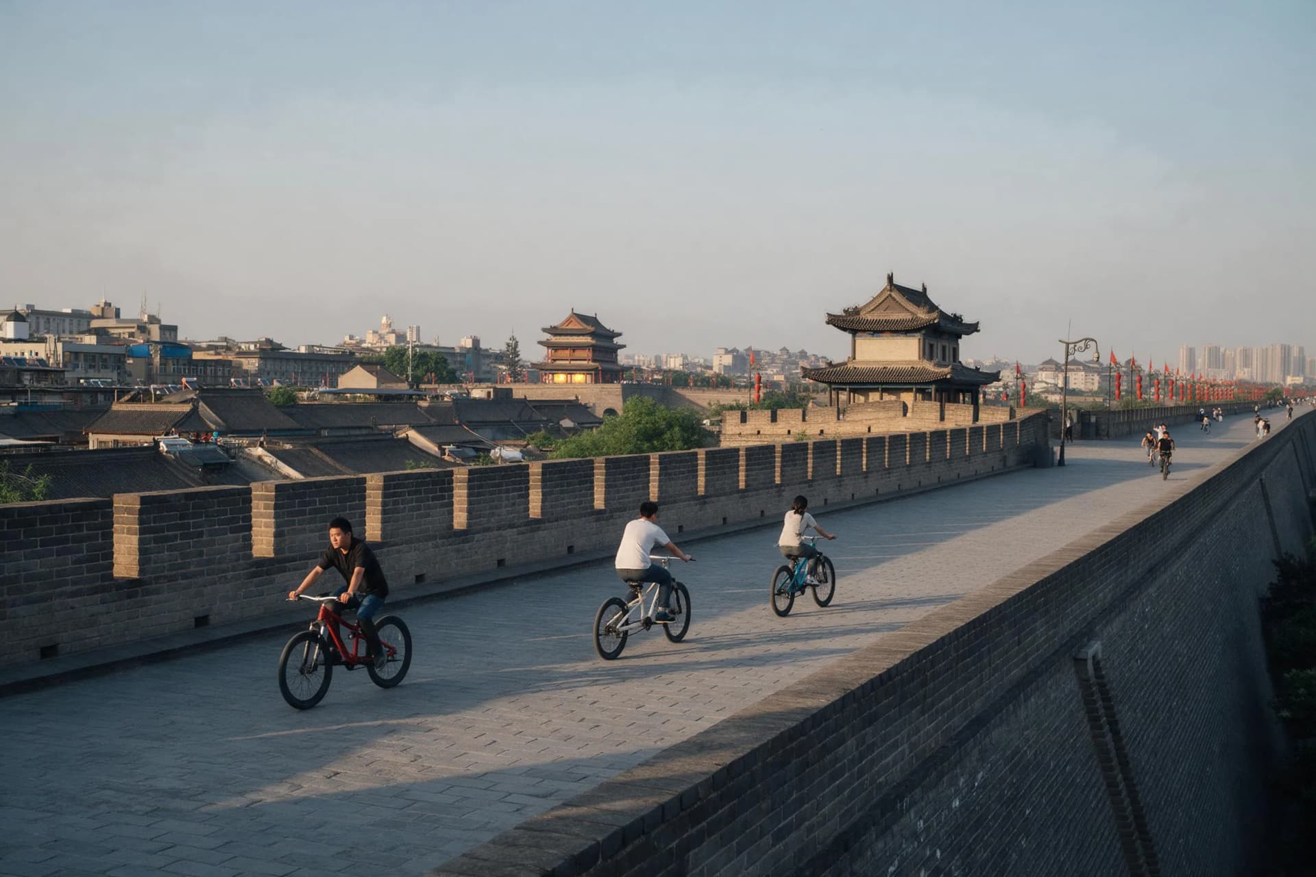 Cyclists on top of Xi'an's Ming dynasty city wall at dusk, with the lit South Gate tower and old town rooftops behind